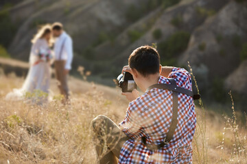 wedding professional photographer takes pictures of the bride and groom in nature in sunny day, man...