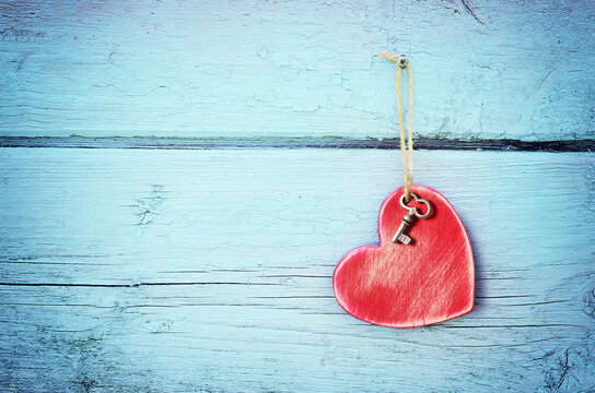 Bronze key and red wooden heart hanging on antique teal blue old wood door. Valentines Day
