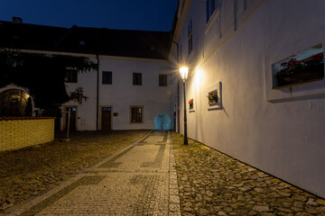 light from a lit street light in a city street at night and in the background is an old monastery from the 12th century and leaves on the ground in autumn in the center of Prague in the Czech Republic