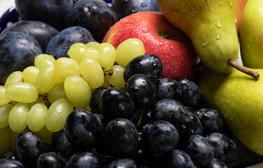green and dark grapes with red apple and green pears on a background of plums close-up. Vitamin Fruit Plate