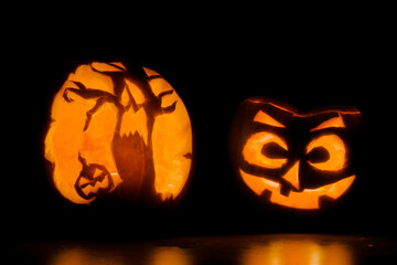 Two intricately carved halloween pumpkins lit by candle tea lights