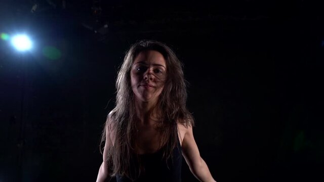 passionate female dancer is dancing in dark studio, waving hair and hands, medium portrait shot