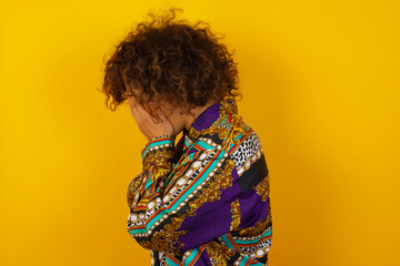 Obraz premium Sad young Caucasian woman wearing casual clothes standing against yellow background covering his face with hands and crying.