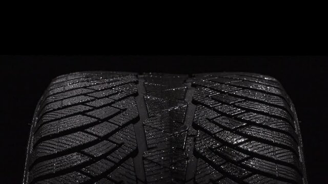 Wet Sports Tire Tread. Loop. The geometric pattern of the wheel in water droplets slowly rotates towards the viewer. Drops sparkle on the black rubber on a black background