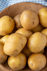 Aerial view small yellow potatoes in wooden bowl, with selective focus, with blue checkered cloth, vertical