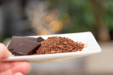 Women hand holding a white plate. On the plate is grated chocolate. In the background is festive bokeh.