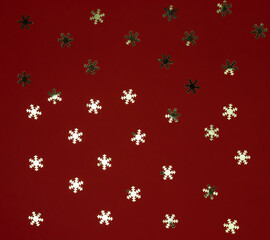 christmas background of sequins in the shape of snowflakes on a red background, winter background, top view, flat lay