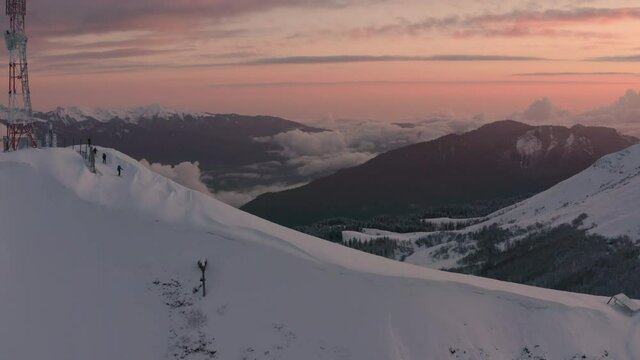Skilled skitour sportsmen ski along ancient Aibga ridge cell tower with high mountain peaks against red sunrise sky with soft clouds aerial panorama. People in evening sunset.