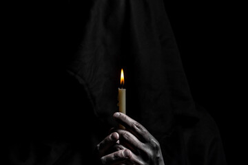 Young catholic nun is holding candle in her hands. Focus on candle. Face is blurred. Photo on black background.