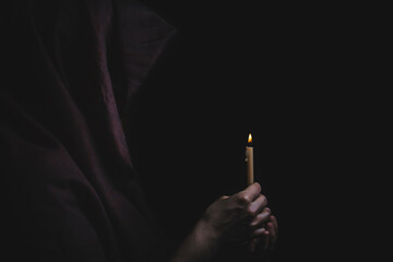 Young catholic nun is holding candle in her hands. Focus on candle. Face is blurred. Photo on black background.