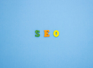 The word SEO on a blue background of wooden multicolored letters.
