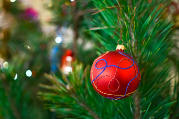 Fototapeta na wymiar Red ball on green spruce branches on a blurred background. Christmas and New Year decorations. A bauble on the tree. Shallow depth of field