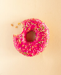 Nibbled bright pink doughnuts with icing and topping on a light yellow back