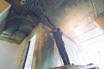 Worker is installing the electrical wires on the ceiling that is the part of internal wiring in...