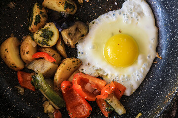 Brekfast fried eggs with vegetables in a frying pan, top view