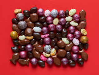 Colored candies of different shapes on a red background, close up, view from above