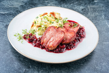 Traditionelle gebratene geräucherte Kablszunge aufgeschnitten mit Kartoffel Püree und Preiselbeeren Relish angeboten als close-up auf einem klassik Desing Teller