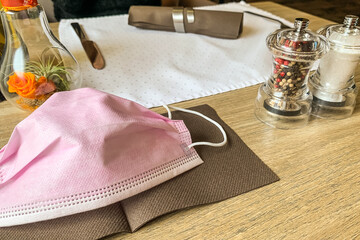 Pink surgical mask on the napkin in a restaurant Concept of new normality