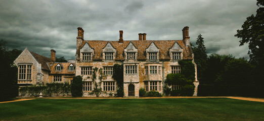 Panoramic, spooky old English manor house with lawn trees. Dramatic cloudy and overcast sky 