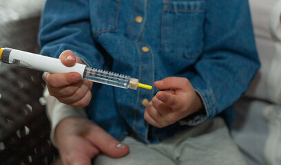 A little girl is holding a syringe with insulin. The girl injects herself. World Diabetes Day.