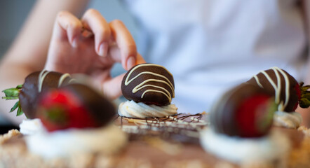 Young woman bakes a cake. Decorating a cake with chocolate covered strawberries