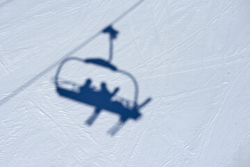 Shadow of the ski lift chair with skiers on the snowy piste surface near Tignes high-altitude...