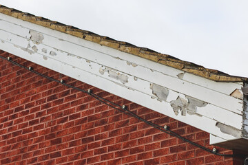 Flaking paint on wooden fascia boards to a side of a brick built building