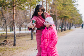 Mom and daughter take a selfie in the park. The child walks with his mother in winter. People in pink clothes take pictures of themselves