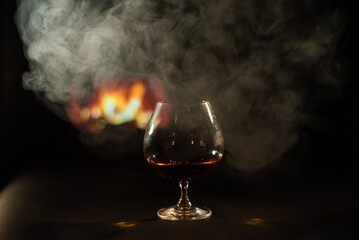 A glass of brandy and cigar smoke in the dark on the background of the fireplace. Gentlemen's club concept