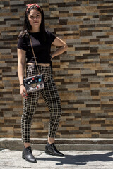 a beautiful young woman wearing casual clothes, standing by a mosaic wall