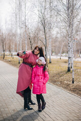 Mom and daughter make stupid selfies. The child walks with his mother in winter and has fun. People in pink clothes take pictures of themselves