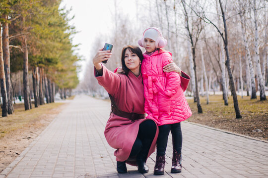 Mom and daughter take a selfie in the park. The child walks with his mother in winter. People in pink clothes take pictures of themselves