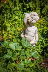 Grungy vintage cherub statue eating grpes in overgrown garden