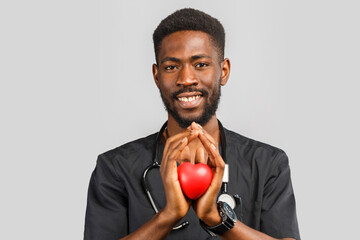 young professional african doctor cardiologist with stethoscope holding red heart in hand, standing against gray background. disease prevention. scheduled inspection