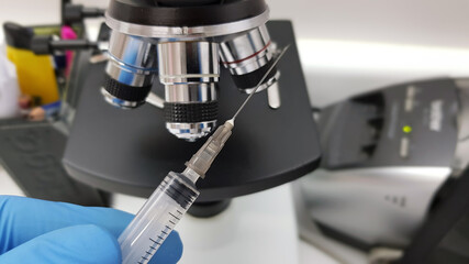 Doctor preparing syringe in medical setup. In the background a microscope. Vaccination concept