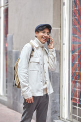 Stylish man walking down the street wearing white  sweater and jacket on street and using his phone