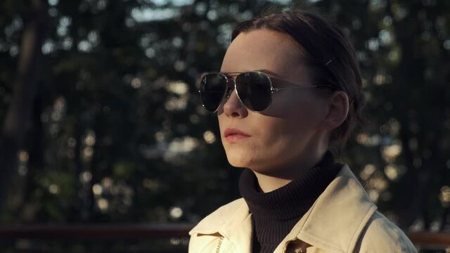 Attractive young woman wearing glasses. Portrait of brunnete girl puts sunglasses on face in sunny autumn day. Side view close up of stylish woman looks away