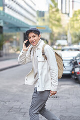 Stylish man crossing the street wearing white sweater and jacket and using his phone