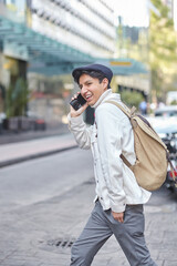 Stylish man crossing the street wearing white sweater and jacket and using his phone