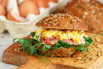 Wholegrain bun with sunflower and flax seeds with bacon, pea sprouts and egg scramble. Gourmet sandwich. Delicious breakfast. brunch. Selective focus