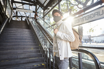 Stylish man wearing mask wearing white sweater and jacket standing on bus station outdoors