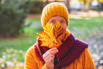 woman in her 50s standing in park in autumn and playing with leaves