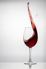 Splash of red wine in a crystal glass on a glazed table silhouetted on white background