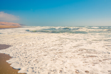 Fototapeta na wymiar Abstract seascape background. Sandy beach, ocean waves, and clear blue sky on background