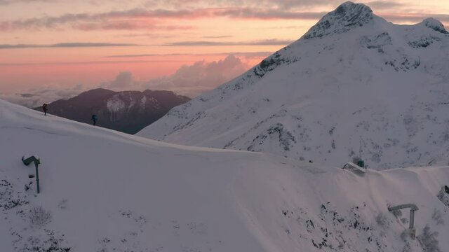 Skilled sportsmen ski along ancient Aibga ridge with high mountain peaks against red sunrise sky with soft clouds aerial panorama. Skitour people in evening sunset.