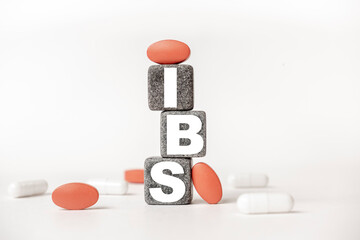a group of white and red pills and cubes with the word IBS Irritable bowel syndrome on them, white background. Concept carehealth, treatment, therapy.