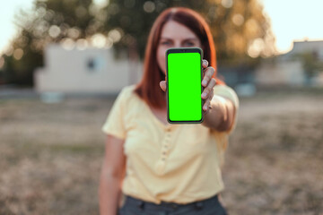 Mockup image of a woman holding and showing black mobile phone with blank screen in the park. Remote control concept. Online training for students. Online shopping