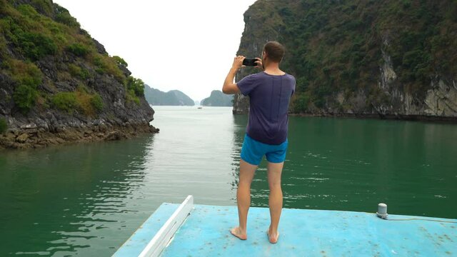 Young man taking photos of beautiful limestone rocks in Ha Long bay