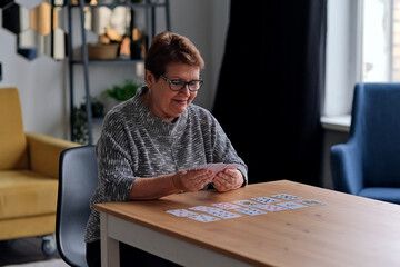 Fototapeta premium senior woman playing solitaire at home. Happy old lady plays an intellectual game