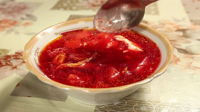 Stir a spoonful of soup in a bowl with mayonnaise. Rich delicious borscht with sour cream. Close-up, selective shot.